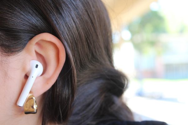 Photo of an AirPod in the ear of a music listener.