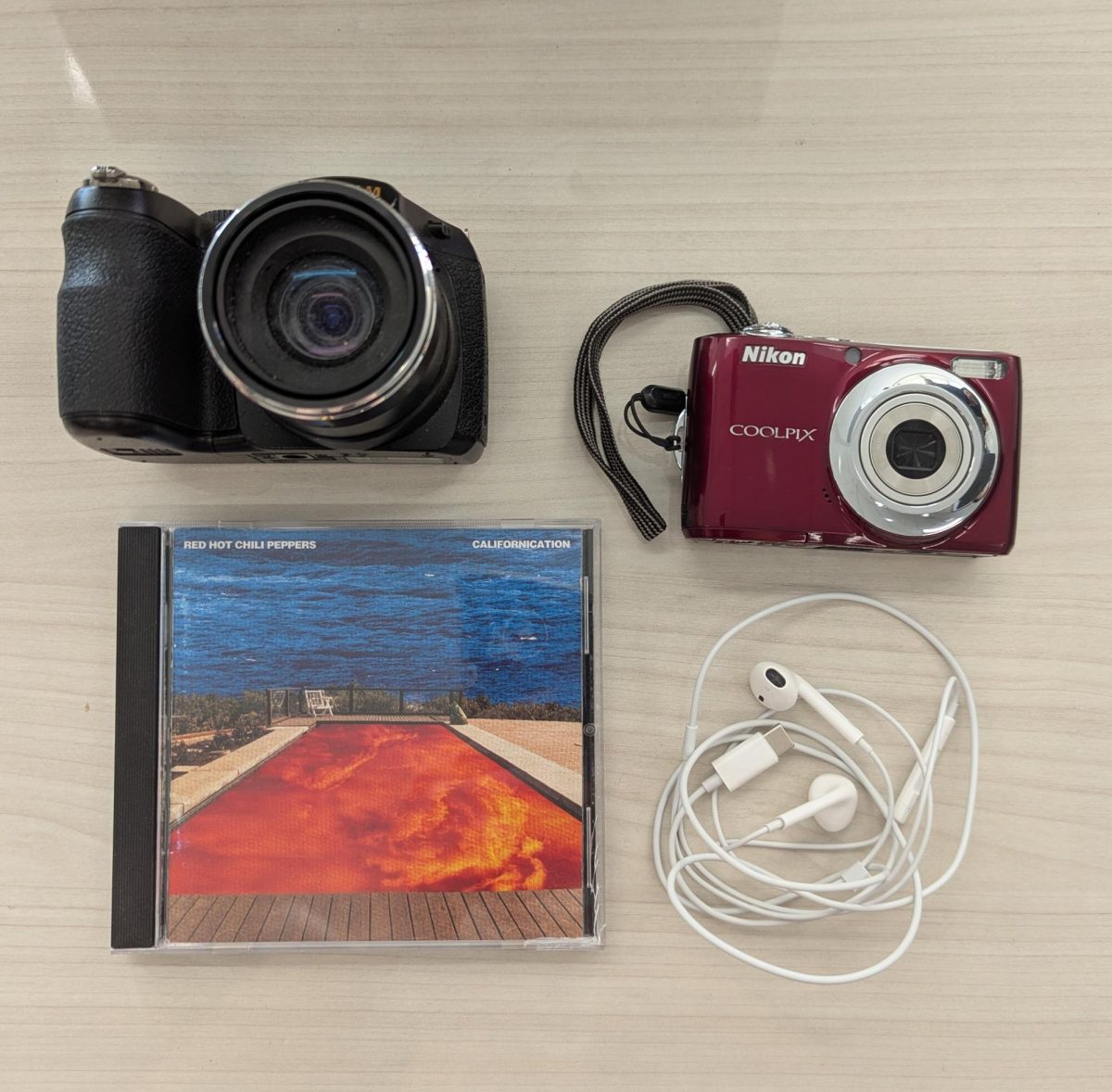 Various forms of tactile technology, including a Fujifilm and Nikon camera, Apple wired earbuds, and a Red Hot Chili Peppers CD